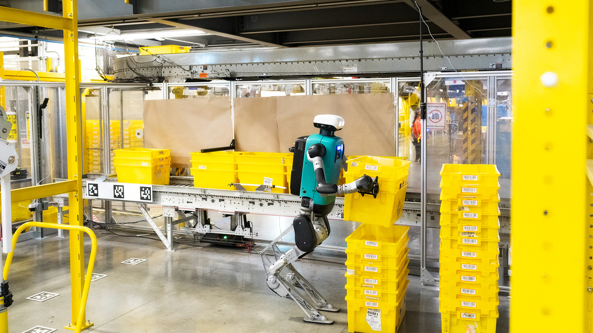 Agility Robotics Digit handles a yellow tote in a guarded fulfillment-site work area