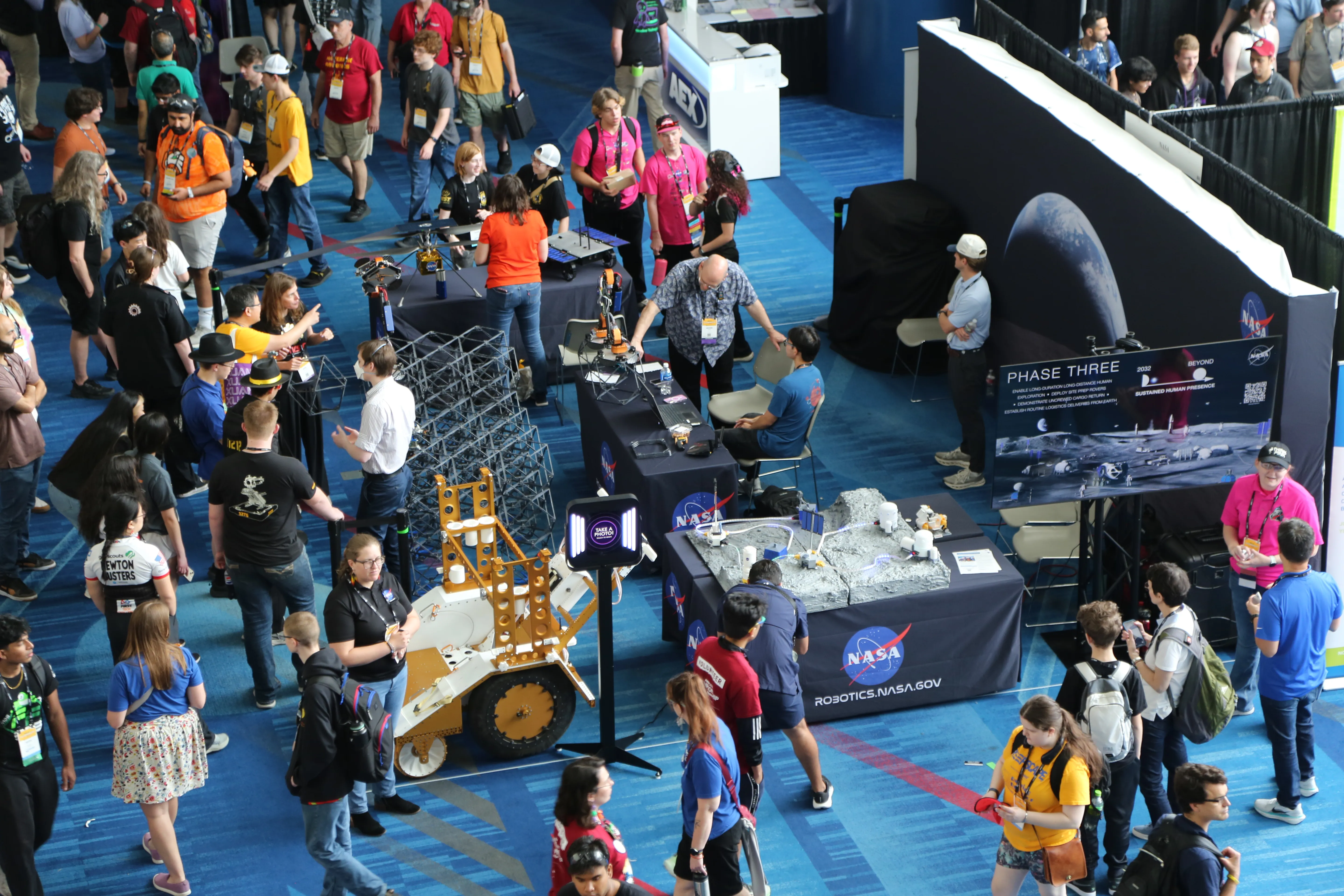 Birds-eye view of a NASA exhibit at the FIRST Robotics Championship in Houston, with a model of NASA’s Moon Base and a lunar sampling cart in the foreground.